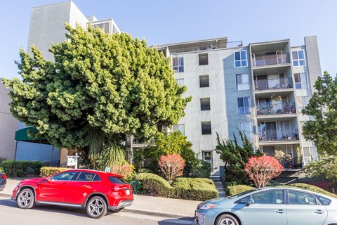 A red car is parked in front of a silver car and a building.