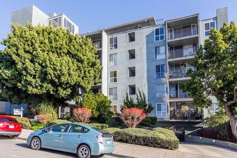 A blue car is parked in front of a grey apartment building.