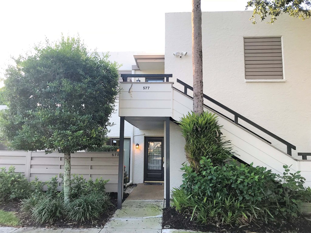 the front of a white house with a tree and a sidewalk