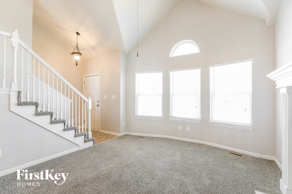 an empty living room with a staircase and three windows