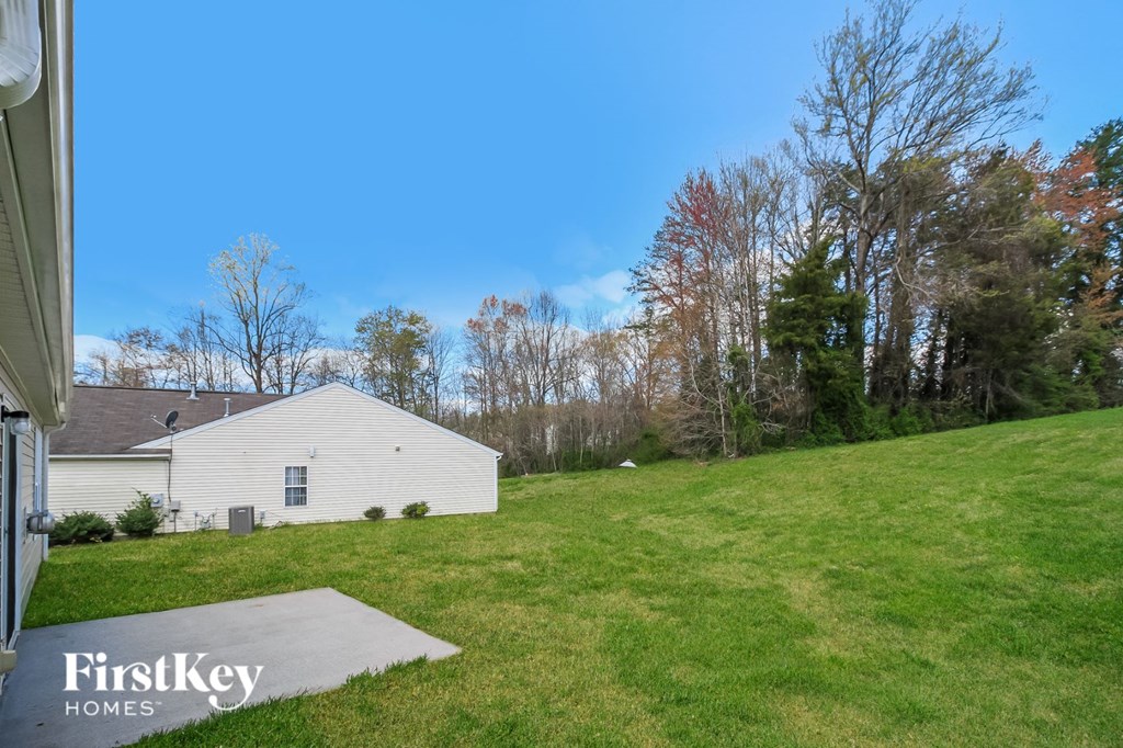 a backyard with a white house and a grassy hill and trees