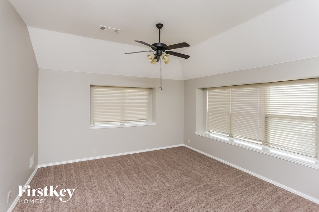 A room with a ceiling fan and two windows.