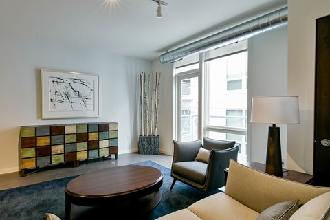 A living room with a brown coffee table, a lamp, a chair, a sofa, and a painting on the wall.