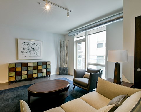 A living room with a brown coffee table, beige couch, and a painting on the wall.