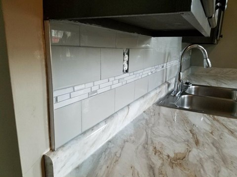 A kitchen counter with a sink and a white tile backsplash.