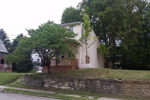 A white house with a brown fence and a tree in front of it.