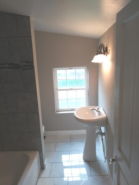 A white pedestal sink in a bathroom with a window.