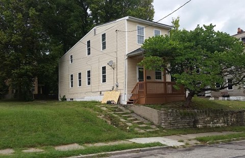 A white house with a brown porch and a tree in front.