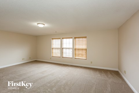 a spacious living room with white carpet and two windows