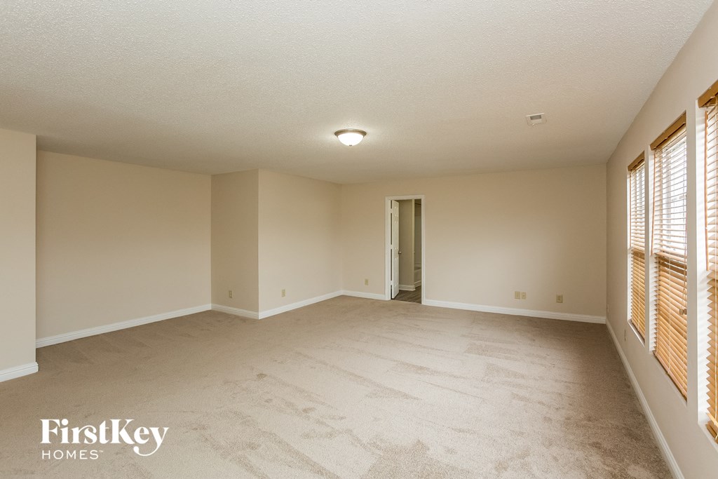 a spacious living room with white carpet and a door to a hallway