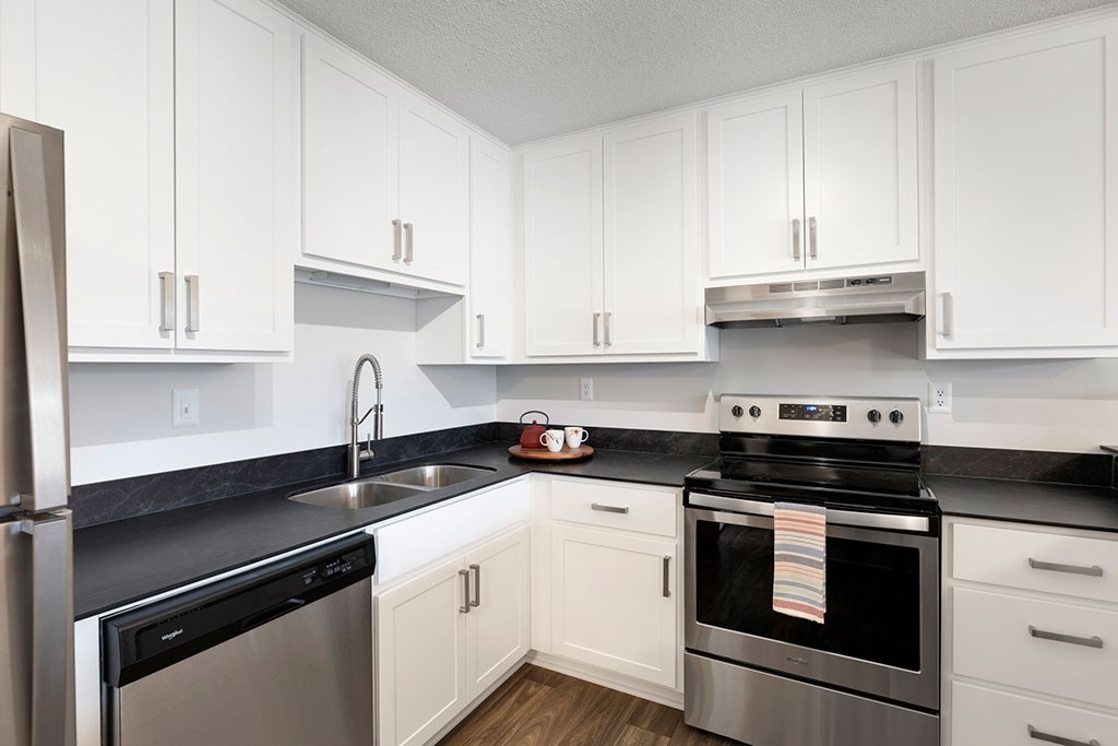 Corner view of kitchen with white cabinetry and stainless steel appliances and black quartz countertops