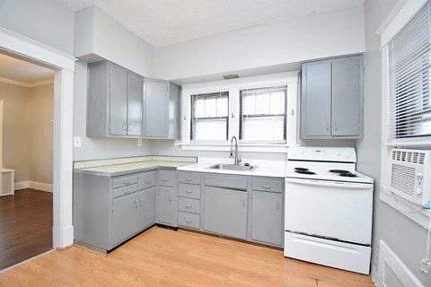 A kitchen with a white stove and grey cabinets.