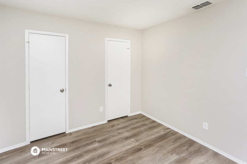 a bedroom with white walls and wood flooring and two doors
