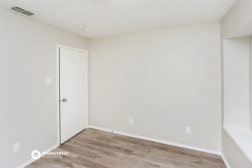 the living room of an apartment with white walls and wood flooring