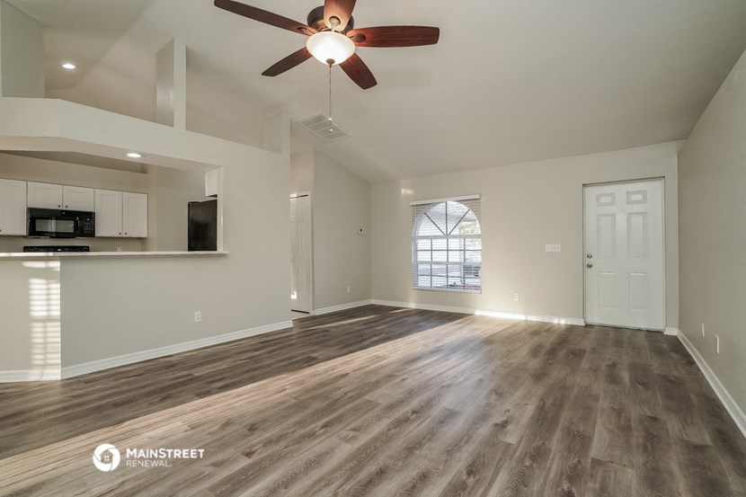 an empty living room with a ceiling fan and a kitchen