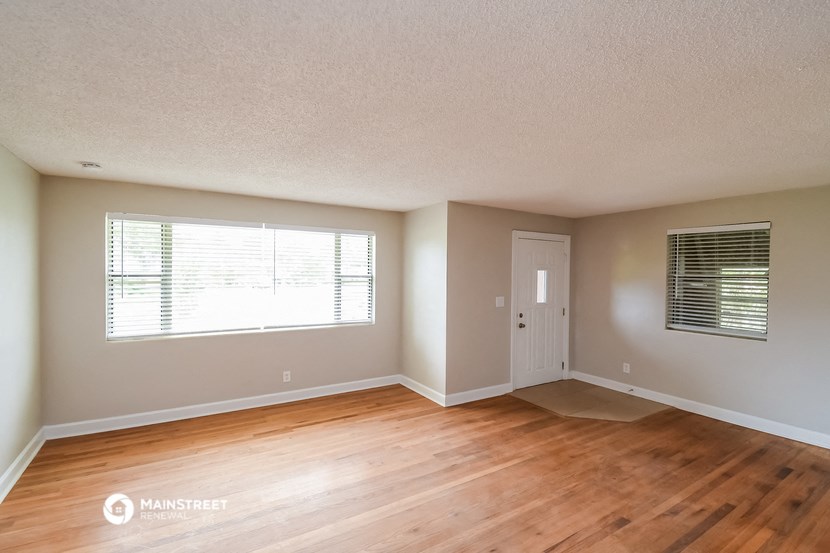 the spacious living room with wood flooring and a window