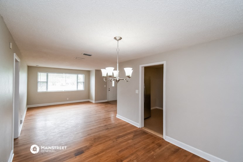 an empty living room and dining room with wood floors and a chandelier