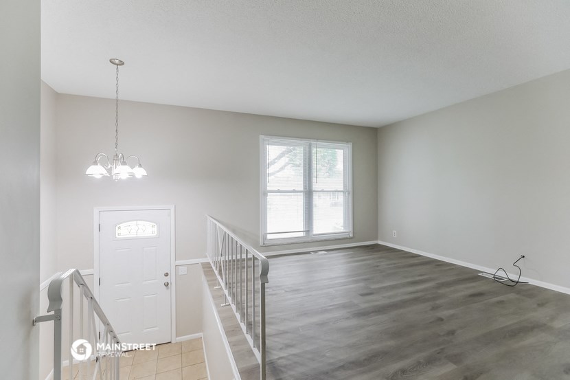 an empty living room with a staircase and a white door