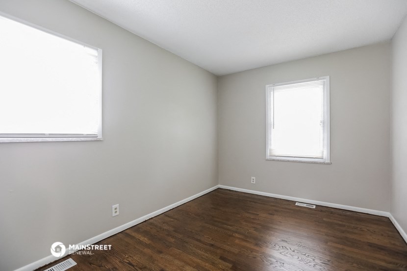 an empty room with wooden floors and two windows