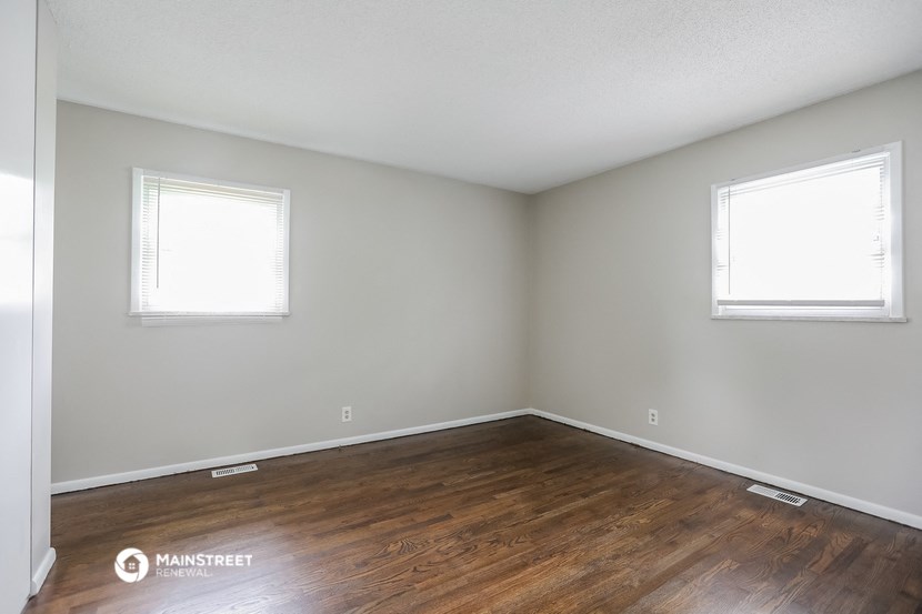 an empty room with wood floors and two windows