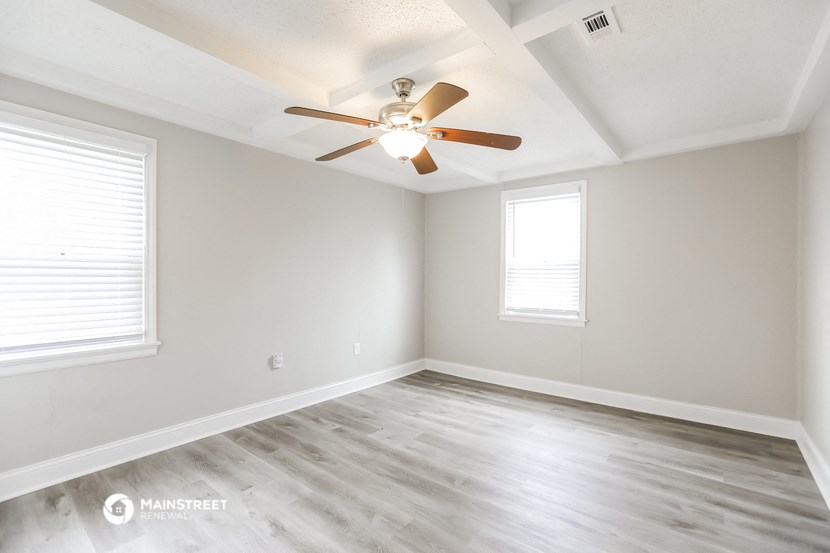 an empty room with a ceiling fan and two windows