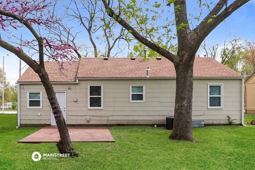 a small tan house with a deck and two trees