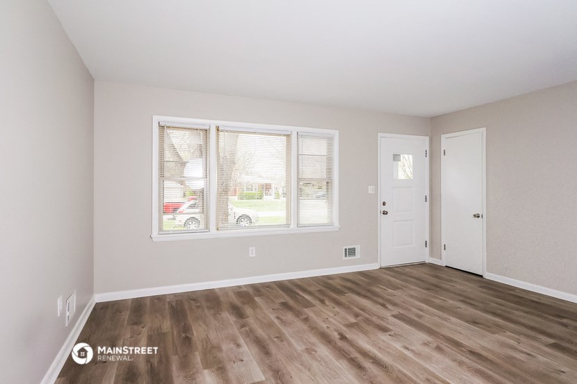 the living room of an apartment with wood flooring and white walls