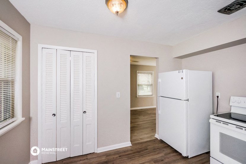 a kitchen with white cabinets and a refrigerator and a door to a hallway