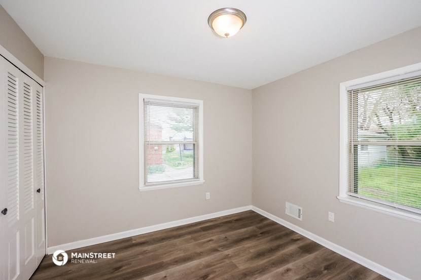 the interior of an empty room with wood flooring and two windows
