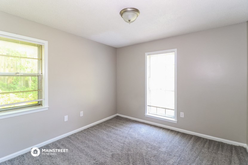 an empty room with carpet and two windows
