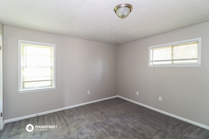 the bedroom of a house with carpet and two windows