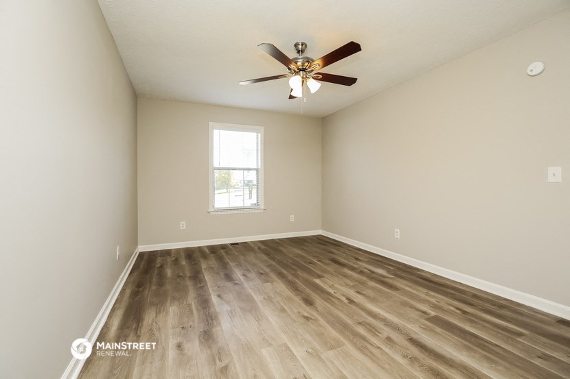 the spacious living room with hardwood flooring and a ceiling fan