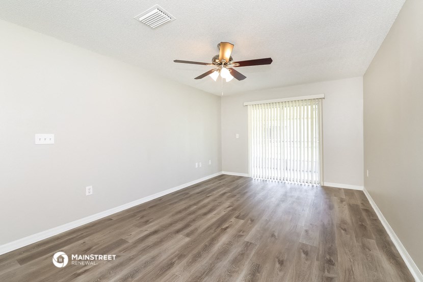 the spacious living room with a ceiling fan and wood flooring