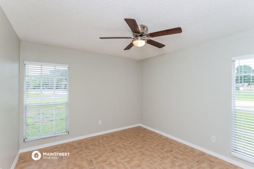 an empty living room with a ceiling fan and two windows