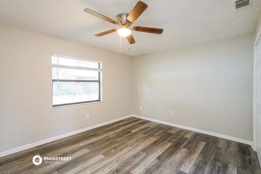 the spacious living room with wood flooring and a ceiling fan