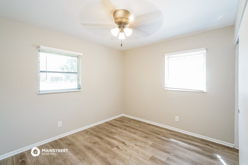 the spacious living room with wood flooring and a ceiling fan