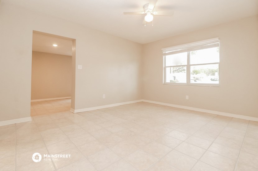 the spacious living room of an empty home with a ceiling fan