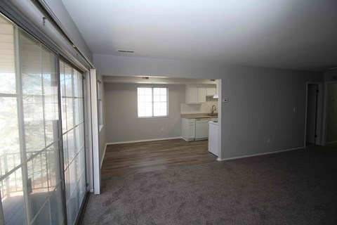 an empty living room with a kitchen in the background