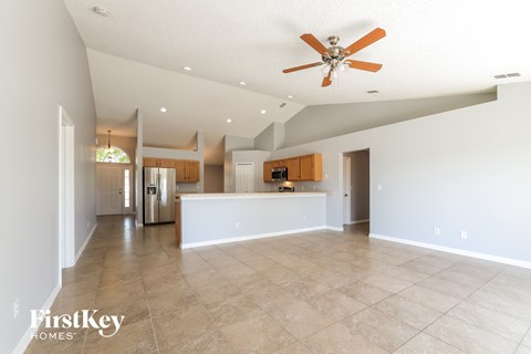 A spacious living room with a ceiling fan and a kitchen in the background.
