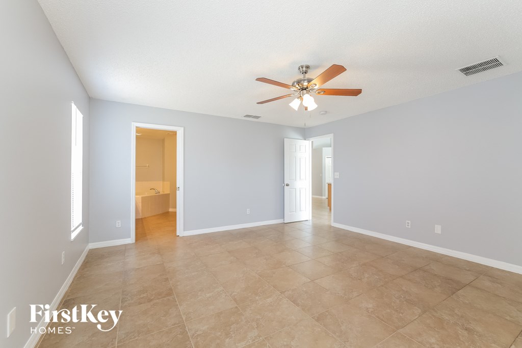 A spacious room with a ceiling fan and light fixture, and a tile floor.
