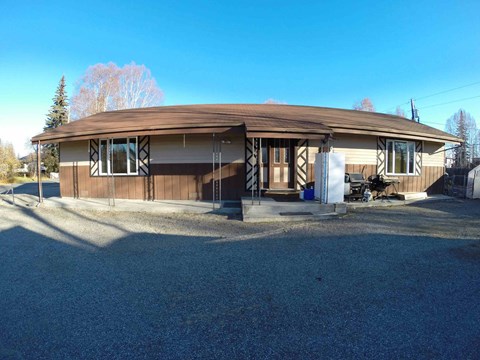 A house with a brown roof and white trim is surrounded by a gravel driveway.