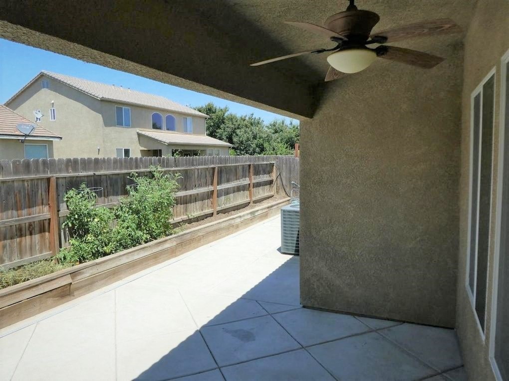 A patio with a ceiling fan and a house in the background.