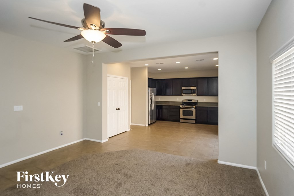 an empty living room with a ceiling fan and a kitchen