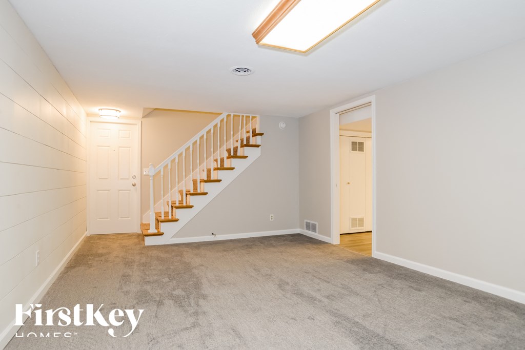 a white carpeted room with a staircase and a white door and a ceiling light