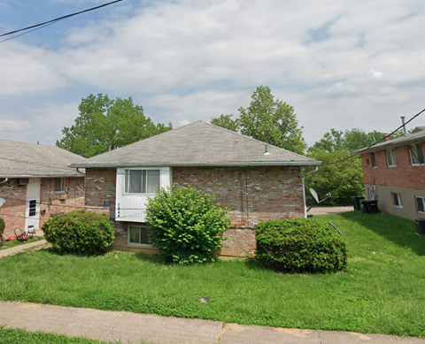 A house with a grey roof and a white window surrounded by green bushes.