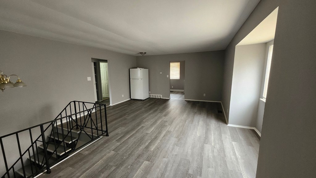 A spacious room with a staircase and a white refrigerator.