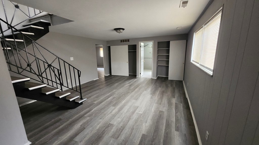 A spacious room with a staircase on the left and a door on the right.