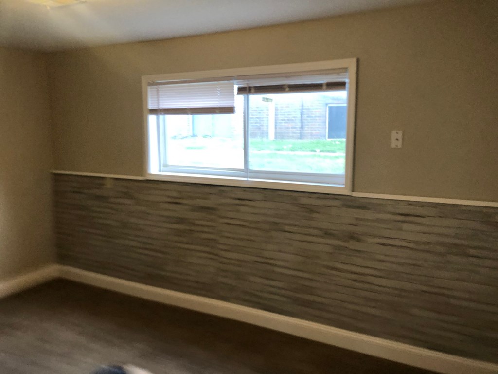an empty living room with a window and a wall with a faux stone accent wall
