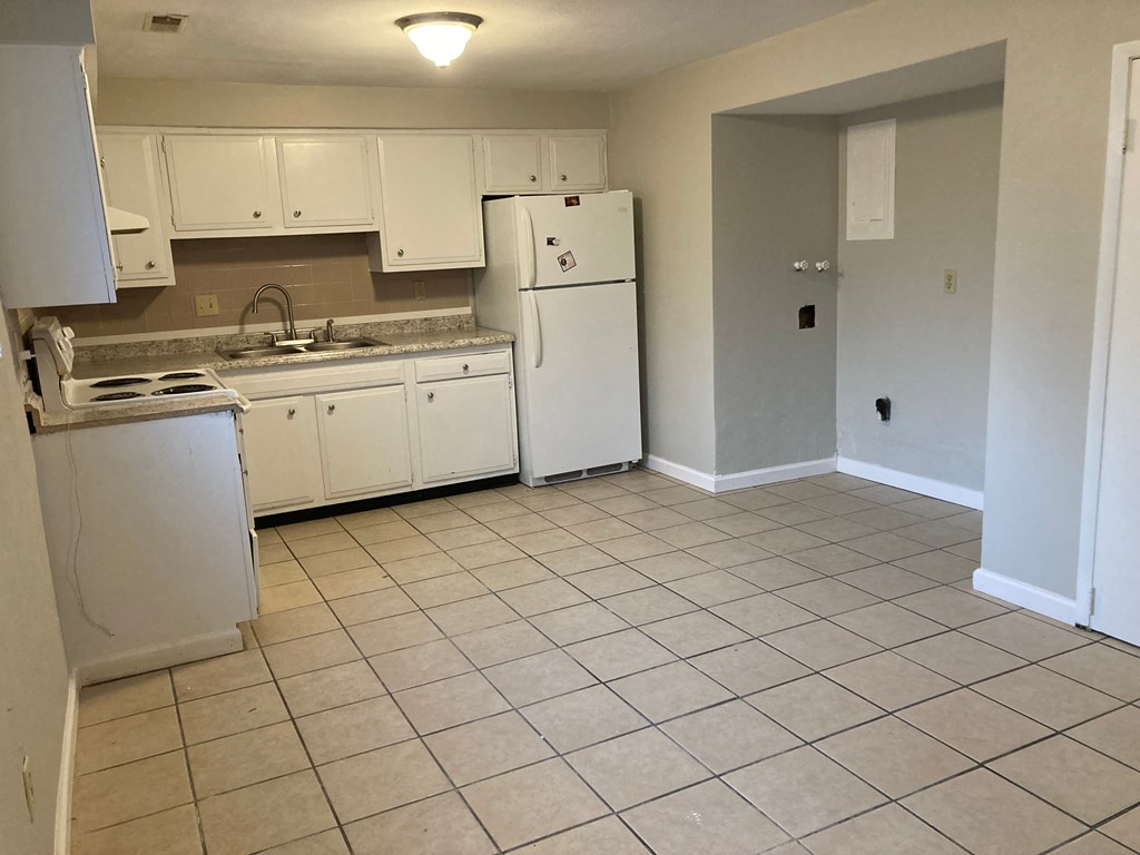 an empty kitchen with white appliances and tiled floors