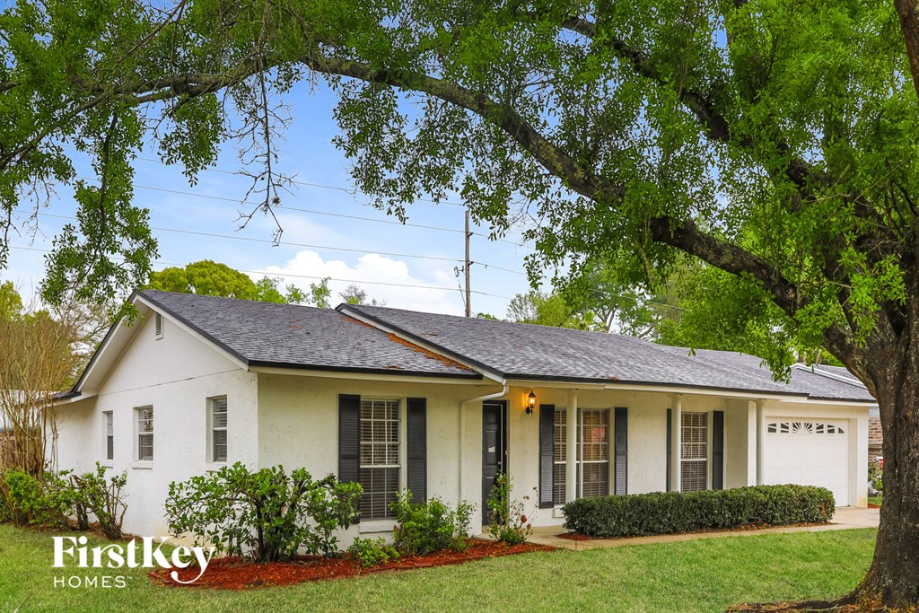 A white house with a black roof and a tree in front.